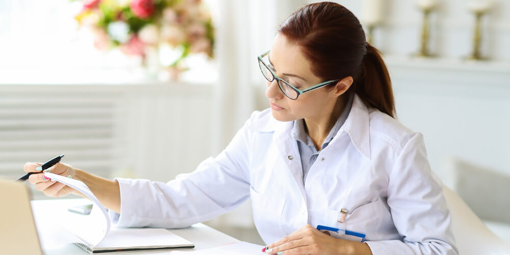Two nurses converse and take notes about medications in the pharmacy.