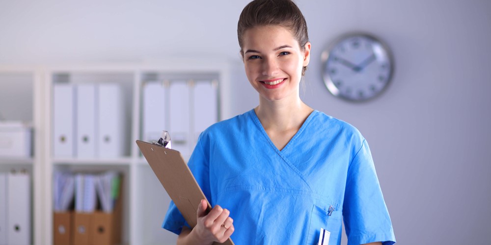 A nursing staff member poses for a photo while holding a grey laptop.