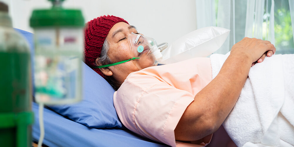 An elderly patient using an oxygen mask and sleeping in a hospital bed