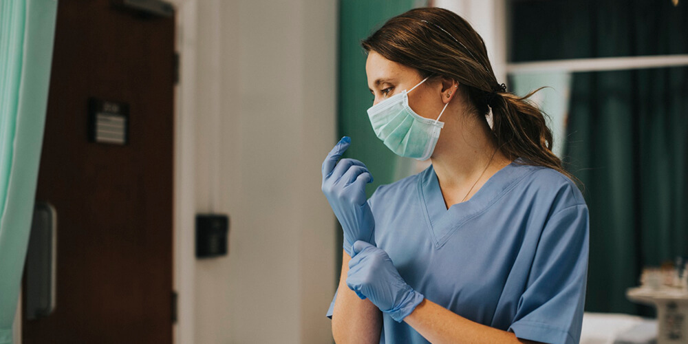 A Nurse professional wearing a mask and disposable gloves in their workplace.