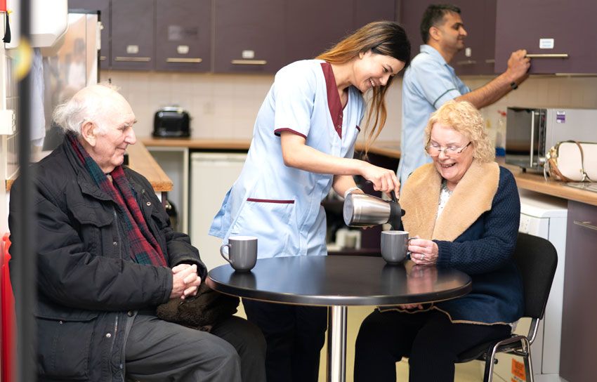 A nursing staff offers coffee to elderly people in the care facility.