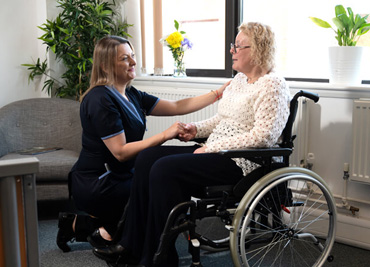 A healthcare worker converses with an elderly woman in a wheelchair.
